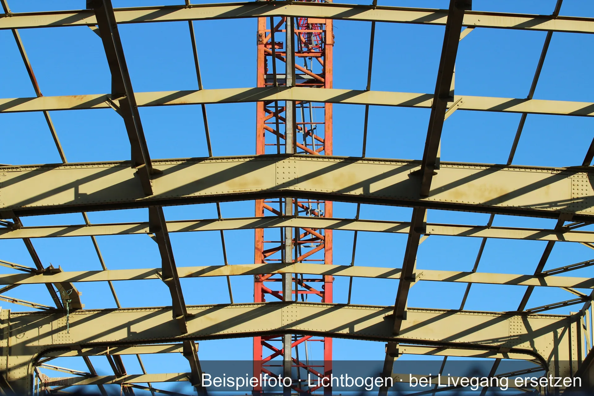 Stahlträger eines Dachtragwerks vor blauem Himmel, dahinter ein Kran.