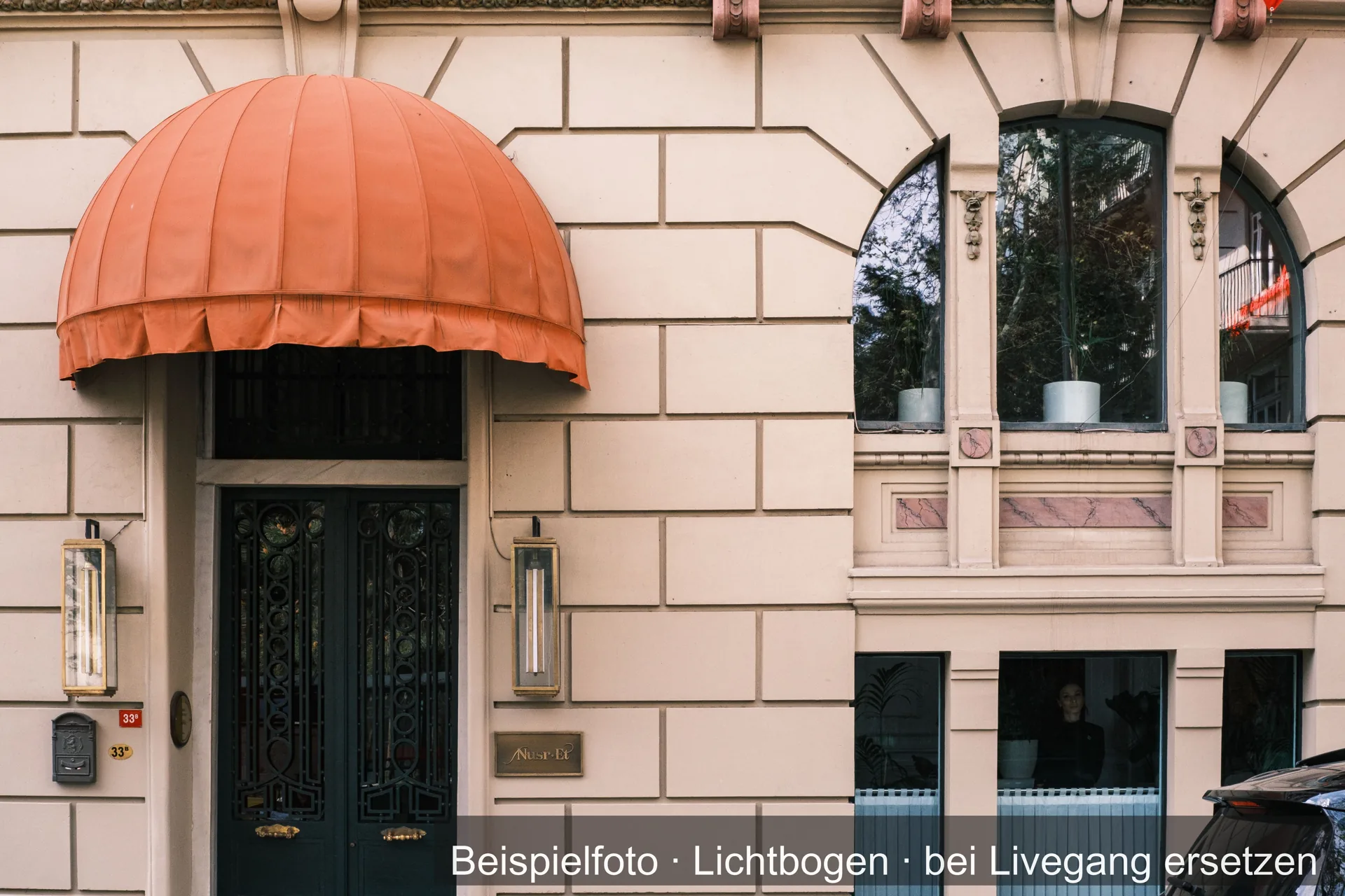 Orangefarbene Korbmarkise über einem Hauseingang in einer Stuckfassade.