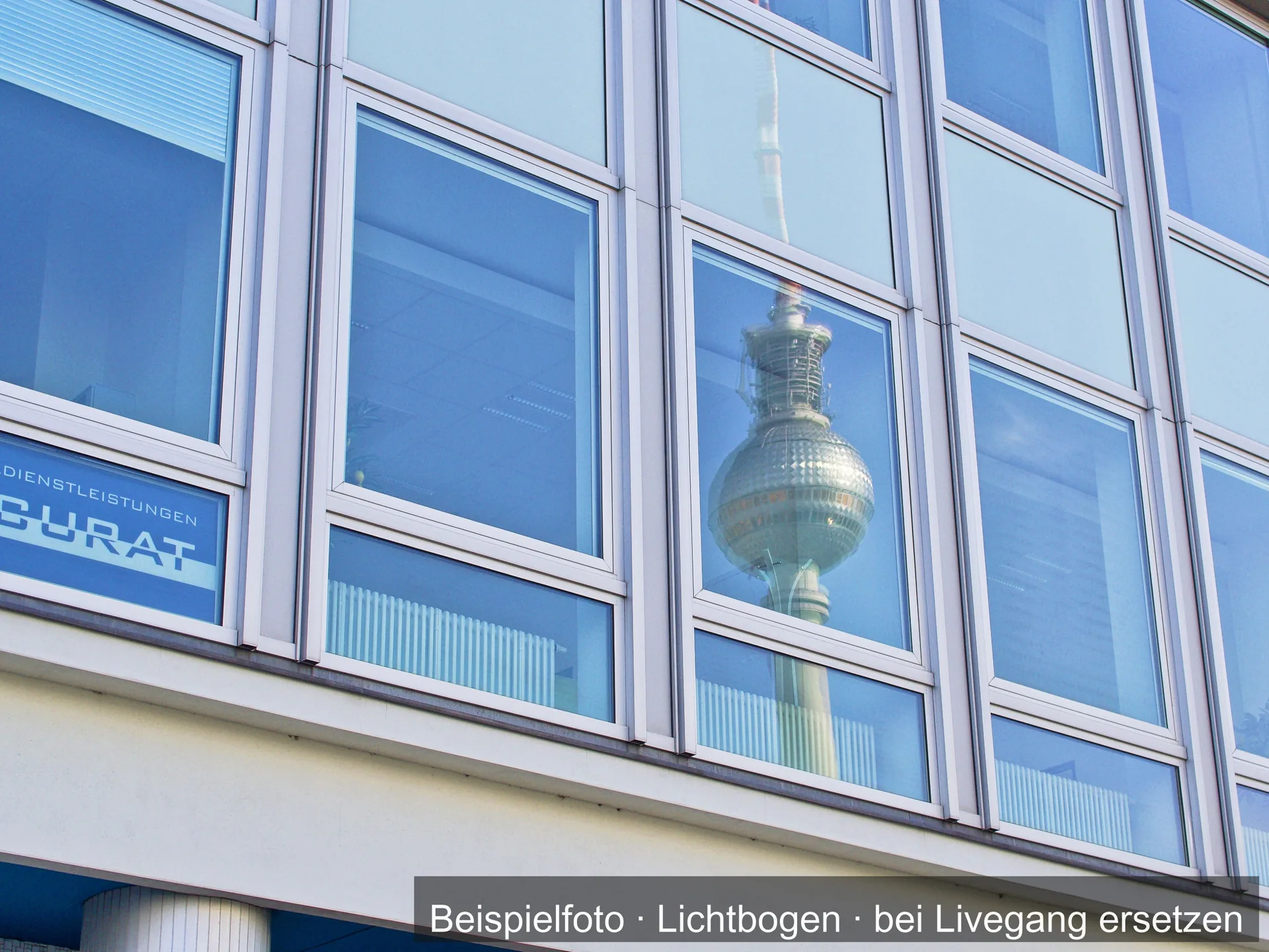 Fensterfassade mit Aluminiumrahmen; in den Scheiben spiegelt sich ein Fernsehturm.