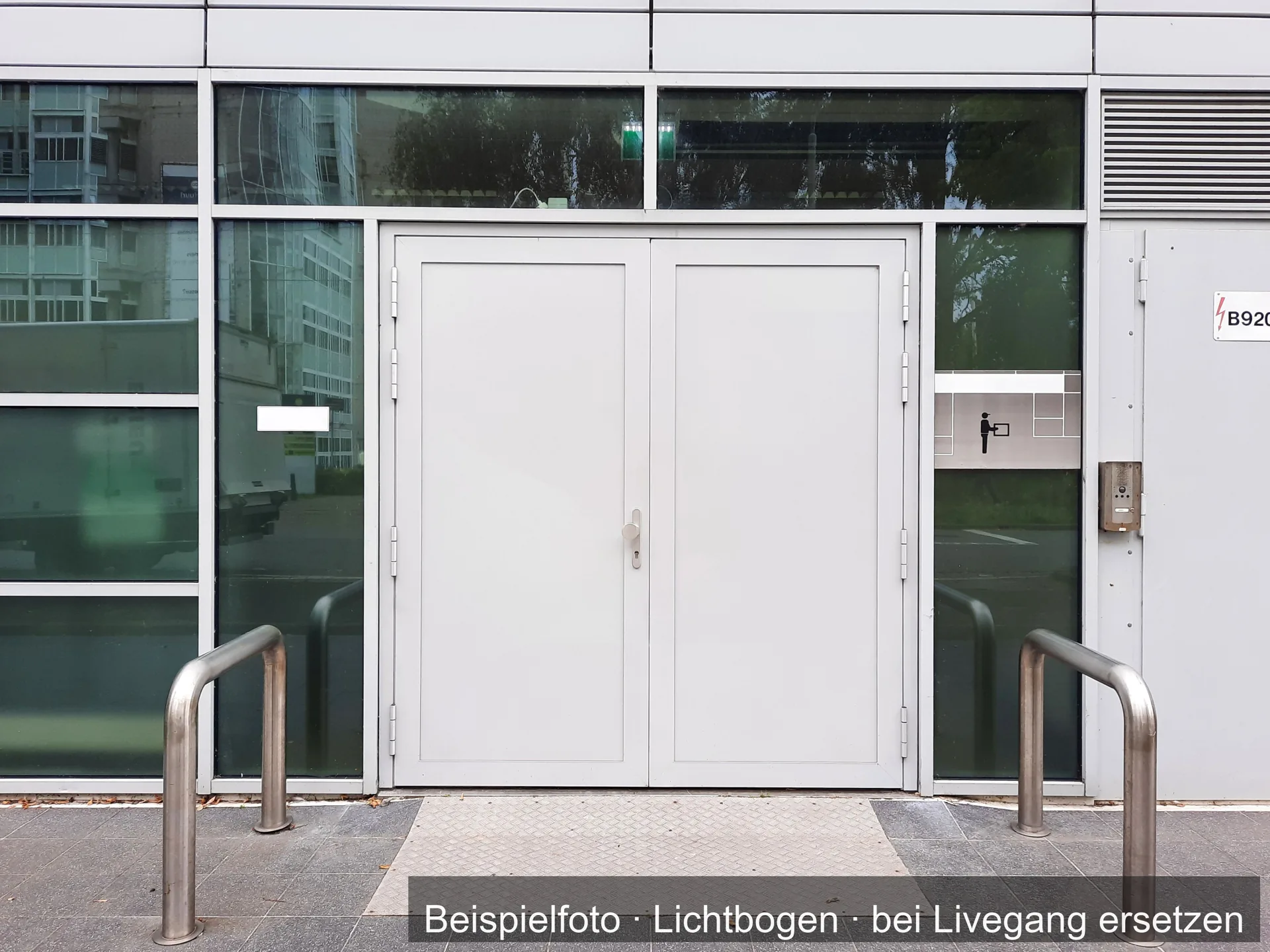 Zweiflügelige graue Metalltür in einer Glasfassade, davor Bügel aus Edelstahl.