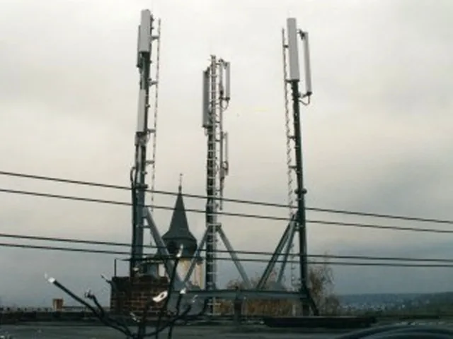 Drei Antennenträger mit Abspannung auf einem Dachstandort, dahinter ein Kirchturm.