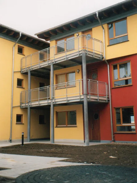 Vorgestellte Stahlbalkone auf Stützen an einem gelb-roten Mehrfamilienhaus.